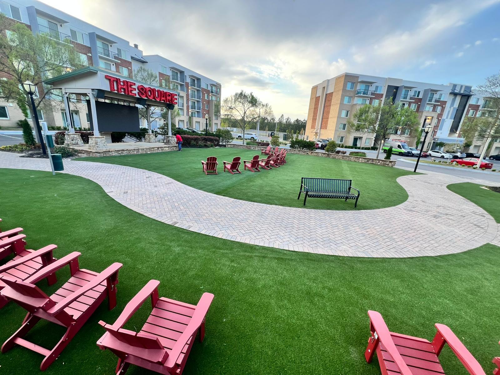 Multifamily community amenity lawn with artificial turf, red Adirondack chairs and paver walkways