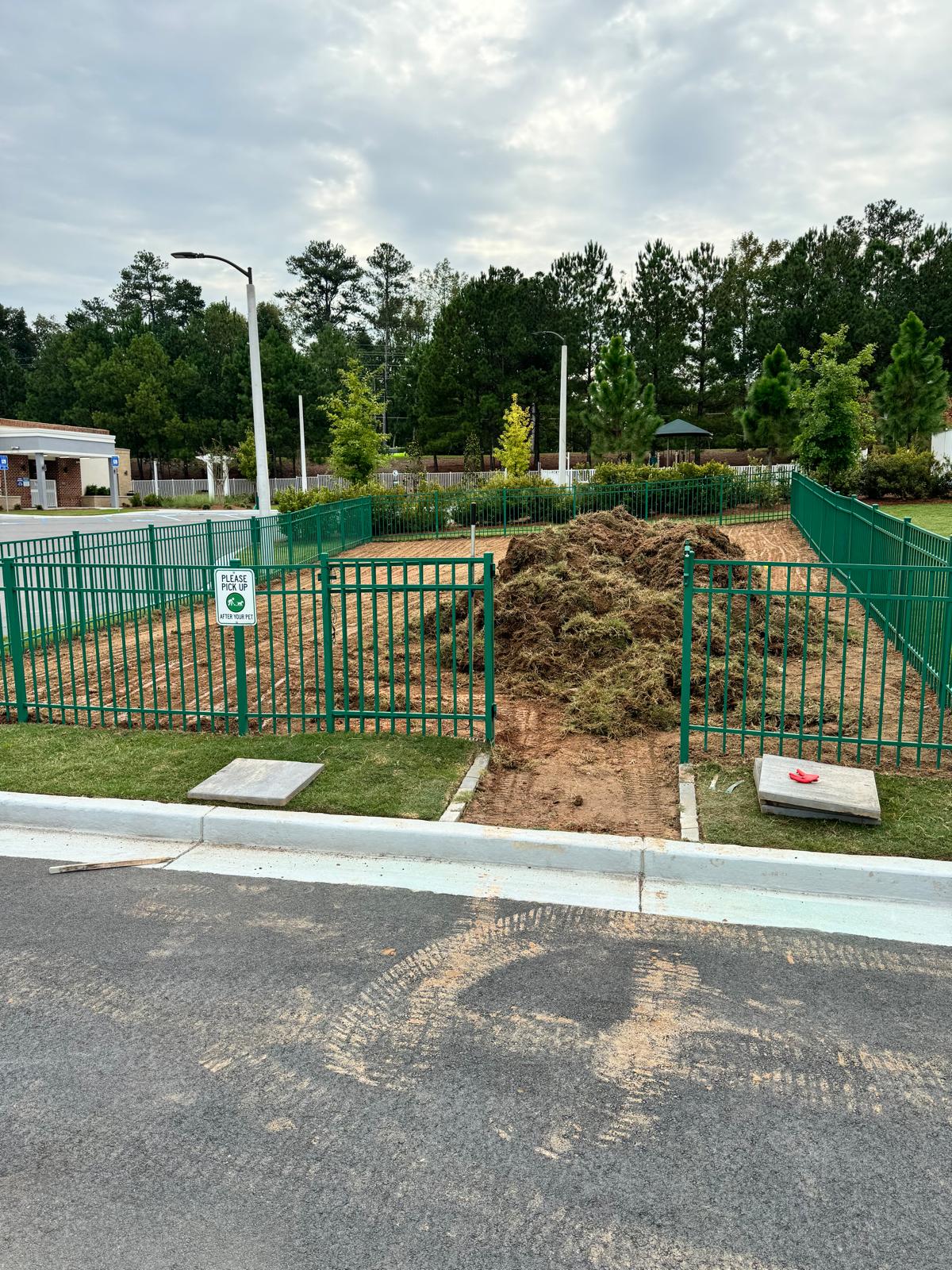 Multifamily dog park during site preparation before artificial turf installation, green fencing in place