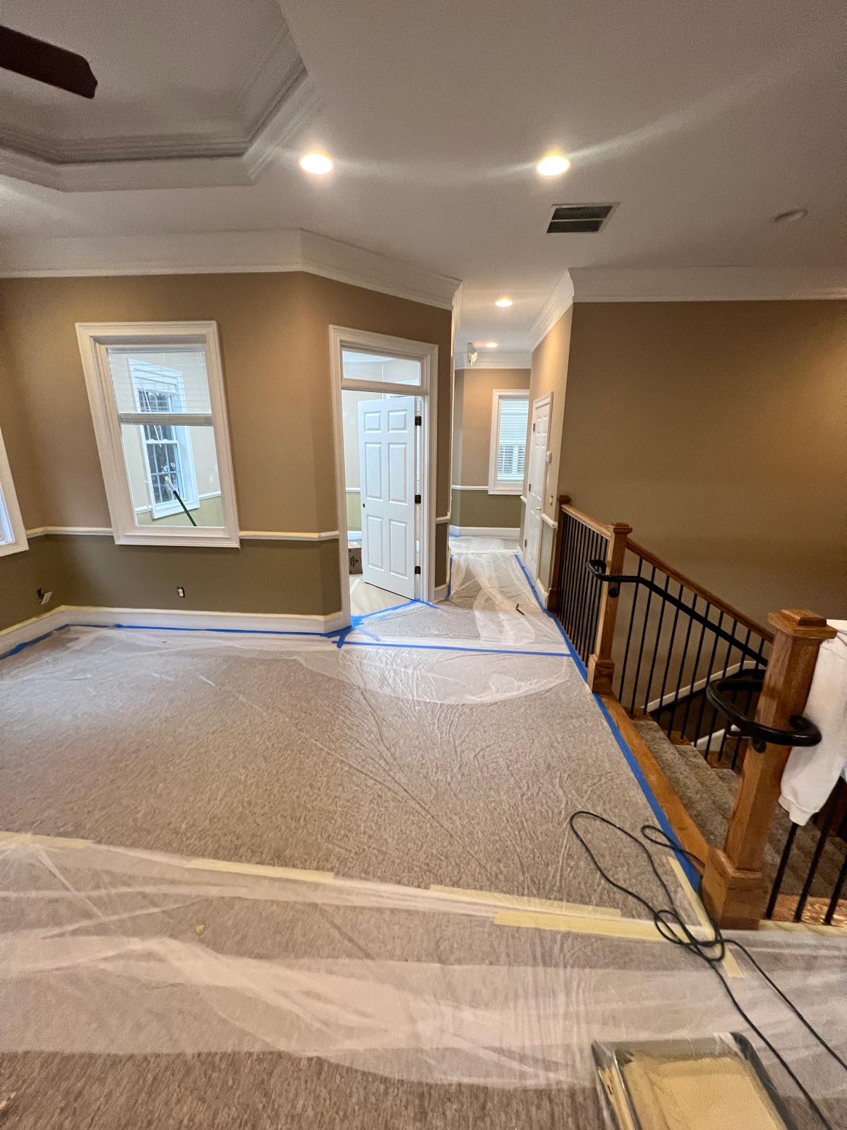 Large office room with carpet and stair landing covered in protective plastic and taped trim before painting