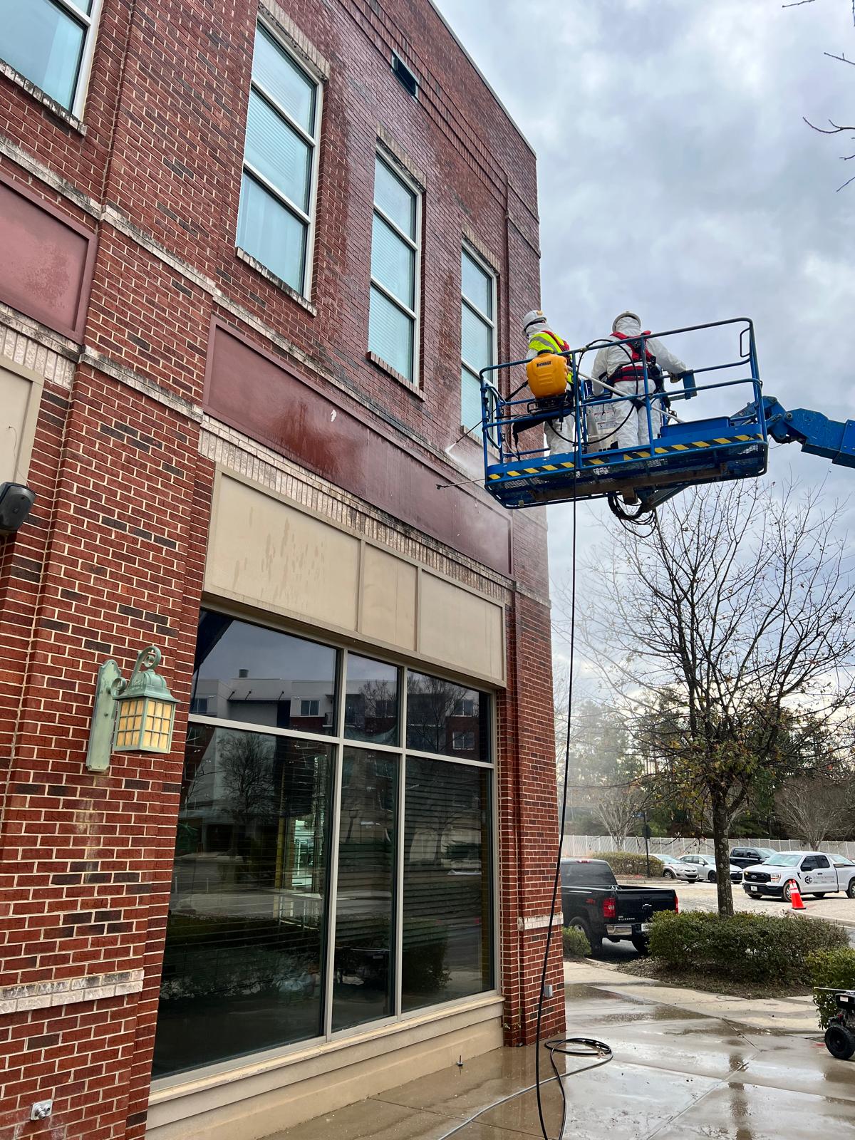DJ7 Solutions crew using an aerial lift to pressure wash the upper exterior of a multifamily building