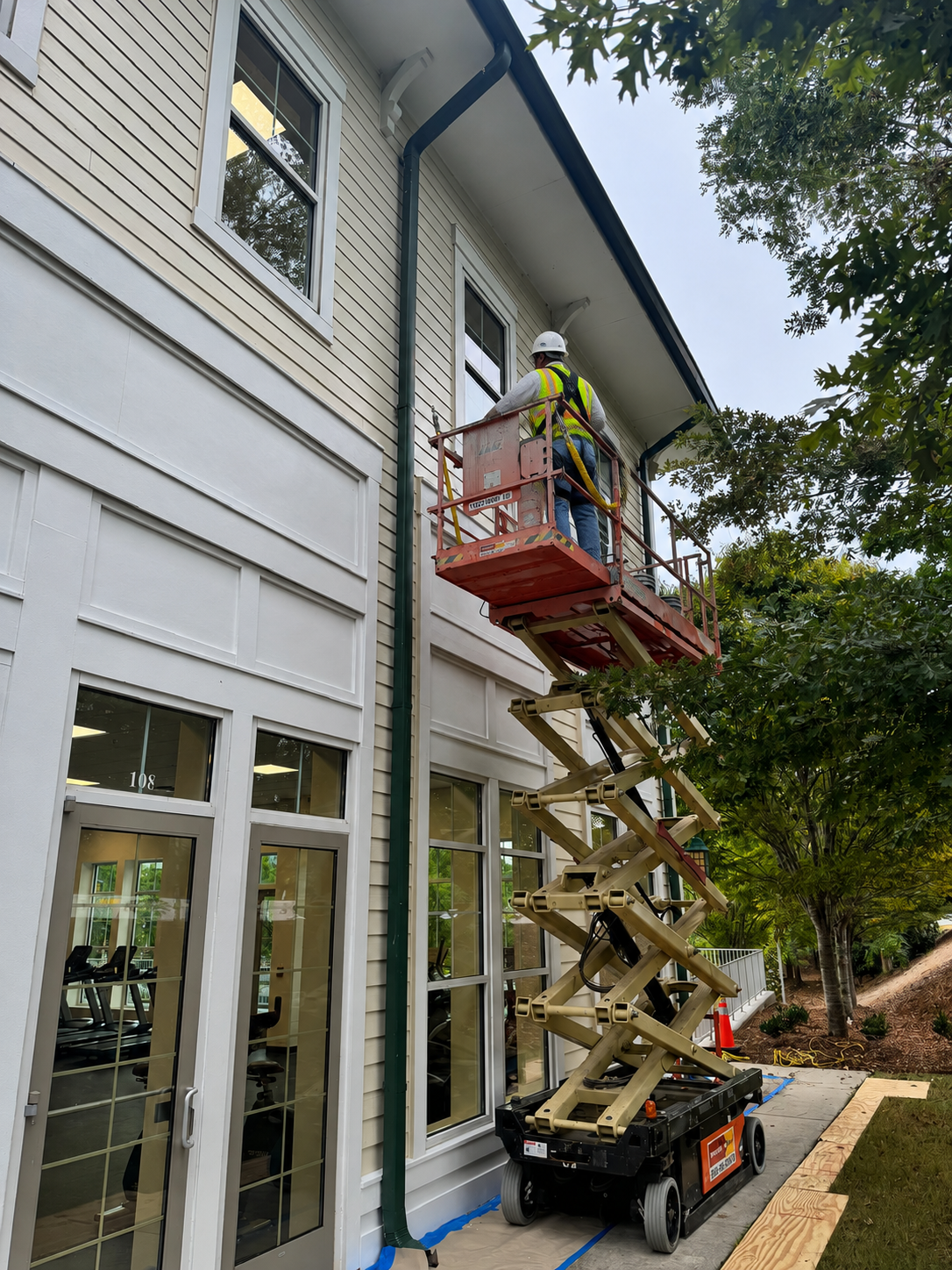 DJ7 Solutions technician on a scissor lift performing exterior painting and maintenance along a multifamily building elevation