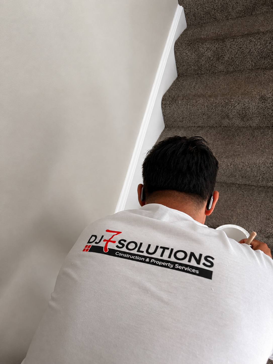 DJ7 Solutions team member painting an interior stairwell wall during a multi-unit apartment turn