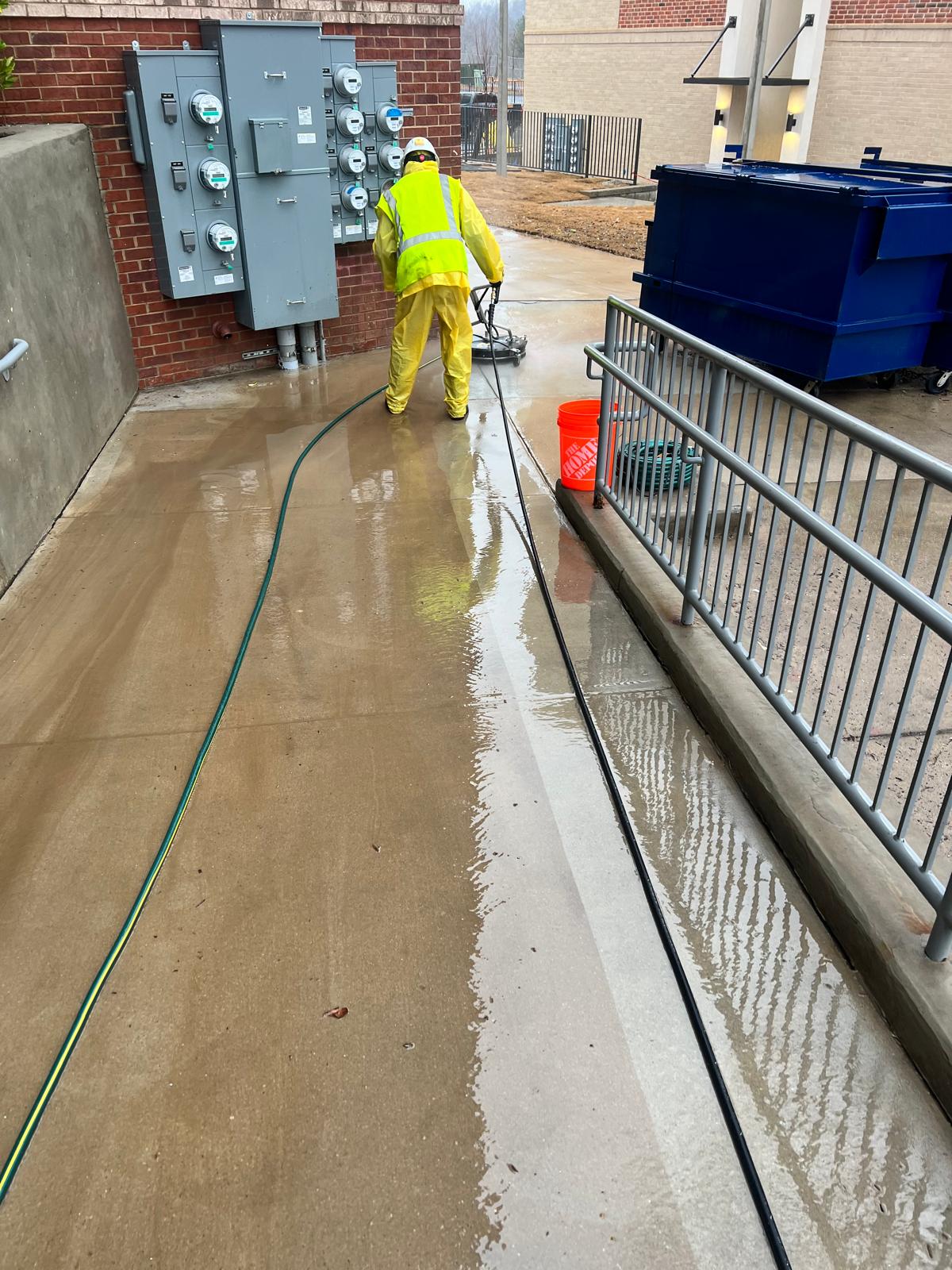Worker using a surface cleaner to pressure wash a concrete breezeway walkway